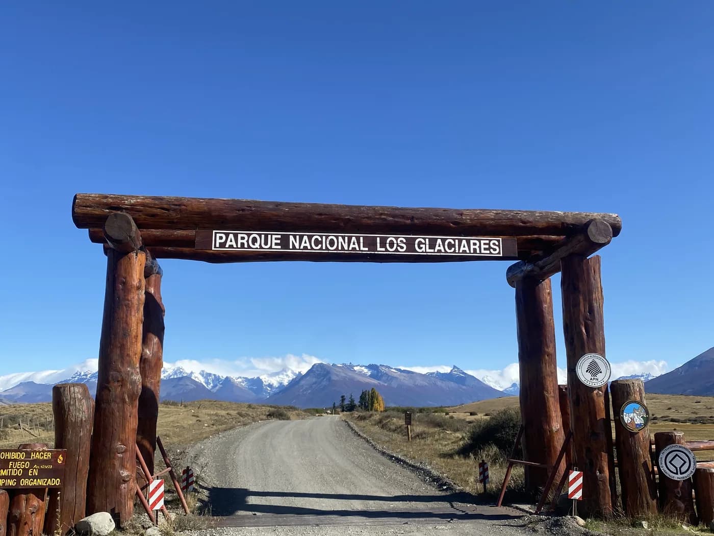 Original photo: the national park's log gateway, the track, and snow-covered peaks behind